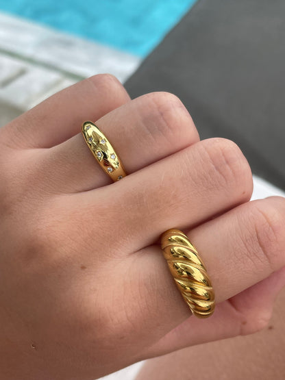 Woman wearing 18k gold-plated star engraved dome ring and croissant twisted ring stacked on hand
