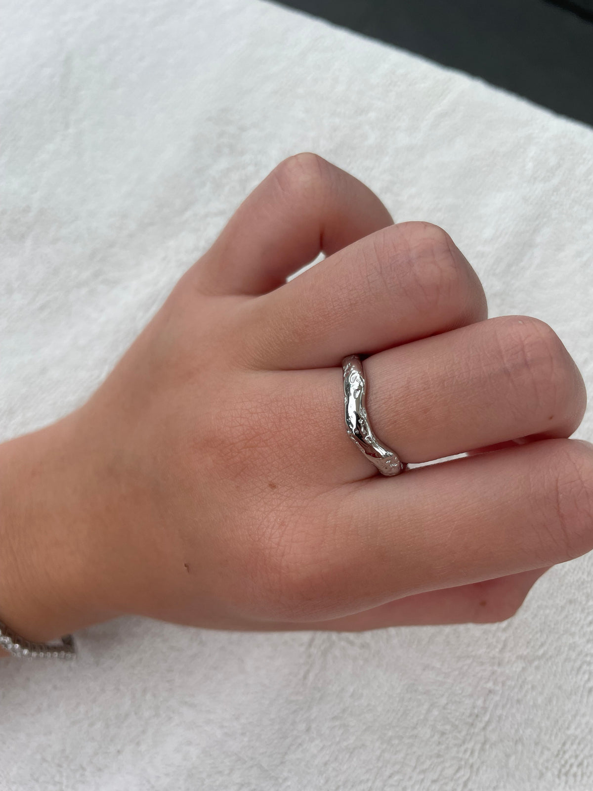 Woman wearing thin silver organic wave ring in textured stainless steel on finger