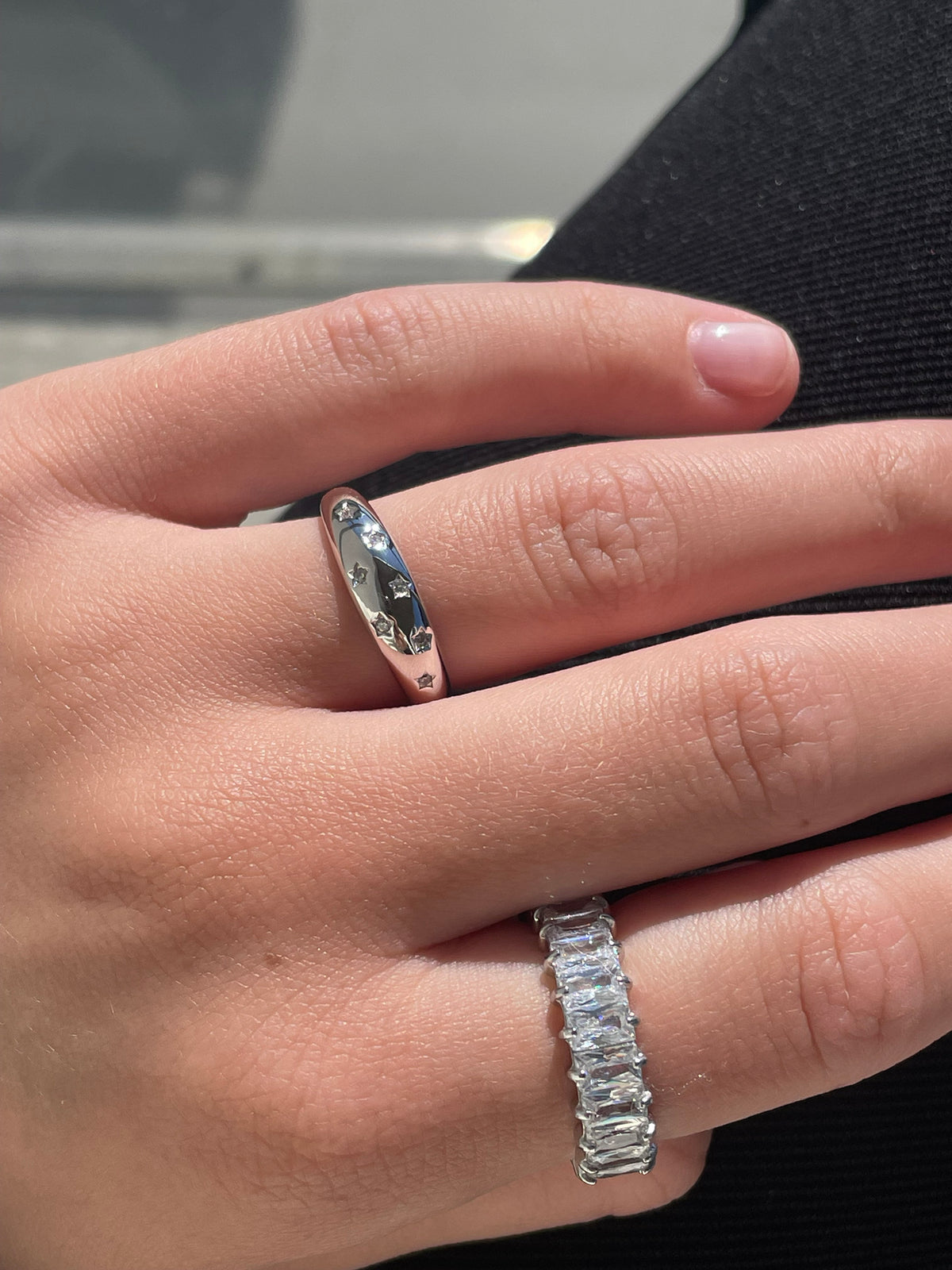 Woman wearing silver star engraved dome ring and baguette cubic zirconia eternity ring stacked on hand
